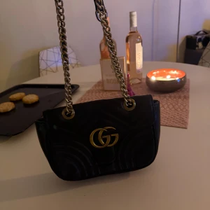 axelväska med kedja - Snygg svart axelväska från  med guldfärgad GG-logga framtill och grov kedjerem. Väskan har quiltad design och är tillverkad i skinn, perfekt för dig som gillar lyxiga detaljer och klassisk stil.