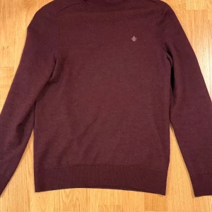 Vinröd stickad tröja från Morris - Säljer en vinröd stickad tröja från Morris  med rund hals och diskret broderad logga på bröstet. Tröjan har lång ärm och ribbade muddar för en clean look. Passar även S