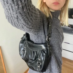 Svart axelväska i skinn med detaljer - Svart axelväska från Accesories bywedins! Perfekt storlek för de viktigaste. Ytterlagret har lossnat lite på axelremmen men inget som syns!