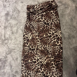 Leopardmönstrad långkjol Tiger Mist - Säljer en långkjol från Tiger Mist med snyggt leopardmönster i bruna och beige toner. Kjolen har en övervikt midja med rynkade detaljer och är tillverkad i ett mjukt, stretchigt material som sitter skönt på kroppen. Perfekt statement-plagg för dig som vill sticka ut.