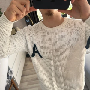 Vit stickad tröja Iconic Sport L - Vit stickad tröja från Iconic Sport(157)i storlek Large. Tröjan har ett stort mörkblått A på bröstet och två mörkblå ränder på ena ärmen. Grovstickad struktur och rund halsringning ger en sportig och avslappnad vibe. Storlek L men passar M(jag är M på bilden). På bilden är jag 176 cm 72 kg 