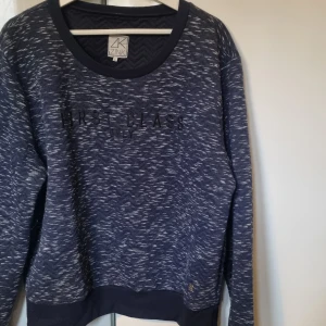 Mörkblå mönstrad sweatshirt från Zink - Säljer en mörkblå sweatshirt från Zink i storlek L med coolt zigzag-mönster och texten 'FIRST CLASS ONLY' broderad på bröstet. Tröjan har ribbade muddar och är långärmad, perfekt för chill dagar. Materialet är mjukt och känns skönt mot huden. Använd ett par ggr.