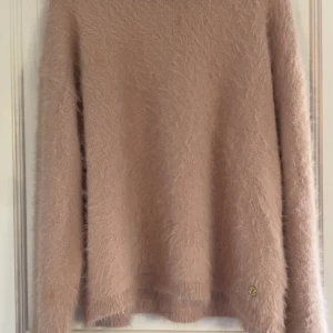 Ljusrosa fluffig tröja Pernilla Wahlgren - Supermjuk och fluffig ljusrosa stickad tröja från Pernilla Wahlgren Design. Tröjan har rund halsringning, långa ärmar och en liten guldfärgad detalj nertill. Perfekt för dig som gillar mysiga och trendiga plagg. PRIS KAN DISKUTERAS