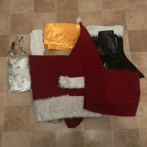 Tomtedräkt med tillbehör - Klassisk tomtedräkt i rött med vita fuskpälsdetaljer, matchande tomteluva, svart bälte, guldfärgad sjal, vita handskar, glasögon och vit peruk. Perfekt för att gå all in på julens alla upptåg! Oanvänd! Kommer med plinga,skägg,vantar,mössa,bälte,väska och glasögon 