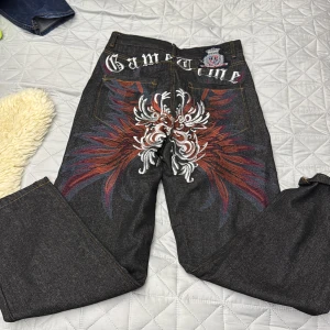 Game Time jeans med broderi - Unika svarta jeans med stort broderat mönster i rött, vitt och blått på baksidan. Snygg textdetalj 'Game Time' både på insidan och utsidan av linningen. Raka ben och klassisk femficksmodell, tillverkade i jeansmaterial.