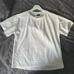 Vit blus med broderade hål  - Säljer en vit blus med korta ärmar och rund hals. Toppen har ett broderat hålmönster över hela tyget 