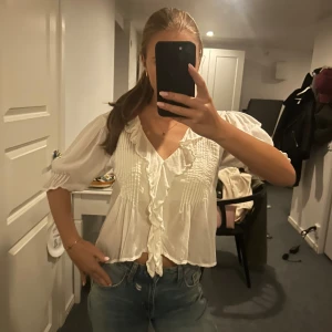 Vit blus med volang och v-ringning - Säljer en söt vit blus med v-ringning och volangdetaljer framtill. Så snygg!