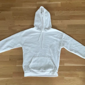 Vit hoodie från SHEIN med huva - Säljer en stilren vit hoodie från SHEIN i storlek S. Tröjan har en klassisk huva med snörning och en stor magficka framtill. Tillverkad i mjuk bomullsblandning, perfekt för chill dagar eller när du vill ha en clean look.