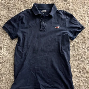 Mörkblå pikétröja från Hollister  - Snygg mörkblå pikétröja från Hollister. Storlek XS men passar S. Hör av dig vid frågor eller prisförslag🙌