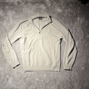 Ljusgrå half zip-tröja Oscar Jacobson - Snygg ljusgrå stickad tröja från Oscar Jacobson med half zip och hög krage. Tröjan är i mjuk ull och har ribbade muddar vid ärmslut och nederkant. Perfekt för lager-på-lager och stilren look.