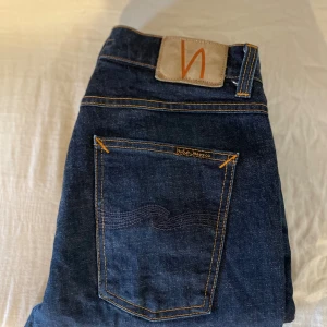 Mörkblå selvedge denim nudie jeans - Snygga mörkblå jeans från Nudie Jeans Co med klassisk femficksdesign och kontrastsömmar. Jeansen har en rak passform och är tillverkade i slitstarkt bomullsdenim. Perfekta för dig som gillar stilrena och tidlösa jeans.