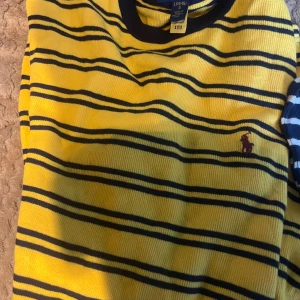 Randig gul pikétröja från Polo Ralph Lauren - Säljer en gul och marinblå randig pikétröja från Polo Ralph Lauren. Tröjan har klassisk rund hals och den ikoniska broderade loggan på bröstet. Perfekt för dig som gillar färg och stil. Materialet är mjukt och skönt bomull.