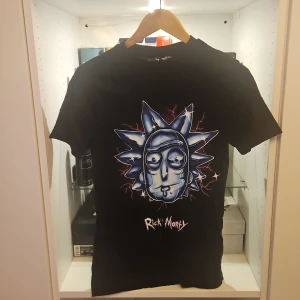 Rick and Morty svart t-shirt - Svart t-shirt med stor blå Rick and Morty-grafik på bröstet och texten 'Rick Morty' under. Klassisk passform och rund hals. Perfekt för fans av serien som vill sticka ut med en cool och unik look.