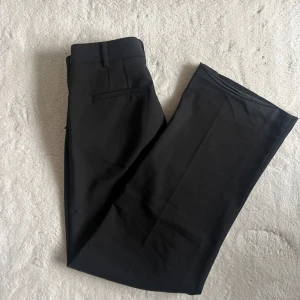 Svarta kostymbyxor från Pulz Jeans - Snygga svarta kostymbyxor från Pulz Jeans med klassisk rak passform och midwaist. Byxorna har bälteshällor, diskreta fickor och stängs med dragkedja och hake. Perfekta för en clean och stilren look.