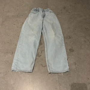 Baggy ljusblå jeans Jack & Jones 152 - Baggy jeans från Jack & Jones i ljusblå tvätt med raka ben och råa, fransiga benslut. Modellen heter Baggy Alex och har klassisk femficksdesign, knapp och dragkedja i midjan samt justerbar resår. Perfekt för dig som gillar avslappnad stil.