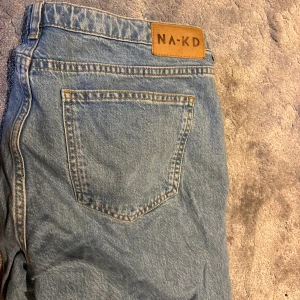 Ljusblå jeans från NA-KD, storlek 40 - Säljer ett par klassiska ljusblå, wide leg, lågmidjade jeans från NA-KD i storlek 40. Jeansen har fickor, gylf med dragkedja och knapp samt en snygg läderpatch med logga bak. Perfekta till sneakers eller boots för en chill look.