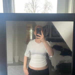 Vit croppad topp med kort ärm - Säljer en vit croppad topp med korta ärmar och rund hals. Toppen har en tight passform och är tillverkad i ett mjukt, stretchigt material som sitter snyggt mot kroppen. Perfekt att styla med jeans eller kjol för en clean look.