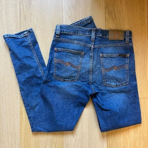 Nudie Jeans Lean Dean blå 28/30 - Snygga Nudie Jeans Lean Dean i mid blue orange med klassisk femficksdesign och orangea sömmar. Jeansen är i stretchigt material med 98% ekologisk bomull och 2% elastan, har smal passform och raka ben. Perfekt för dig som gillar stilrena och bekväma jeans. Hör av dig vid minsta fråga!
