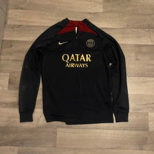 Svarta PSG Nike träningsbyxor - Svarta träningsbyxor från Nike med PSG-logga och Nike Swoosh i guld på framsidan. Byxorna har smal passform, resår i midjan och är tillverkade i ett mjukt och stretchigt material som passar perfekt för fotbollsträning.