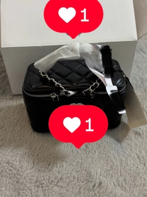 Svart quiltad handväska med kedja - Säljer en svart, rektangulär handväska med quiltat mönster och silverfärgad kedja som handtag. Väskan har dragkedja runt om och en stilren look som passar till många outfits. Perfekt storlek för det viktigaste och snygg detalj till din stil.