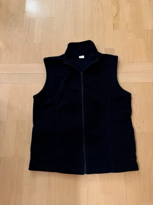 Marinblå fleeceväst med dragkedja - Marinblå väst i mjuk fleece med hög krage och hel dragkedja framtill. Västen har en enkel och stilren design utan synliga detaljer eller mönster, perfekt att slänga på sig när det är lite kyligt. Passformen är normal och materialet känns skönt mot huden.