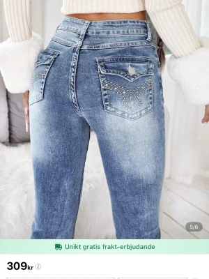 Blå bootcut jeans med detaljer - Säljer ett par blå bootcut jeans med hög midja och snygga broderade detaljer på bakfickorna. Jeansen har en tvättad look och klassisk femficksdesign. Materialet är jeans och passformen är normal med lätt utsvängda ben.