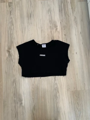 Svart croppad topp från Gymshark - Säljer en svart croppad topp från Gymshark med tryck både fram och bak. Toppen har avklippta ärmar och midja.