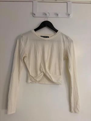 Dam Vit croppad långärmad topp  - Säljer en stilren vit croppad topp från ISTAY med lång ärm och twistad detalj framtill. Toppen har rund halsringning och är i storlek XS. Perfekt att matcha med höga jeans eller kjol.