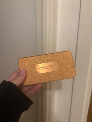 Anastasia Beverly Hills ansiktspalett - Snygg ansiktspalett från Anastasia Beverly Hills i en glittrig guldig förpackning. Paletten innehåller en persikofärgad rouge, en skimrig highlighter och en varm bronzer. Perfekt för att skapa glow och definition. Smidig spegel i locket för enkel applicering. Ord pris 659kr