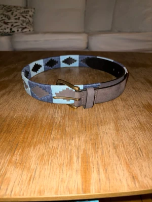 Mönstrat skärp i läder och textil - Säljer ett snyggt skärp med klassiskt mönster i blått, och ljusblått. Skärpet har detaljer i brunt läder. Perfekt accessoar för att lyfta din outfit med lite färg och stil. Storlekar 80,85,90,95,100,105 och 110.