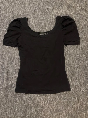 Svart topp med puffärm från Zilhouette - Säljer en svart topp från Zilhouette med puffiga korta ärmar och rundad urringning. Toppen är figurnära och sydd i mjuk bomull, perfekt för dig som gillar enkel men snygg stil. Passar till allt och är superenkel att matcha.