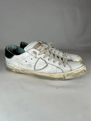 Vita sneakers från Philippe Model - (Nypris 3400kr) tjena Säljer ett par äkta vita Philippe Model sneakers i skinn med grå snörning och svart detalj på hälen. Klassisk låg modell med rund tå och platt sula. Skorna har den ikoniska sköldloggan på sidan och diskreta hål för ventilation.(Size 44-45)