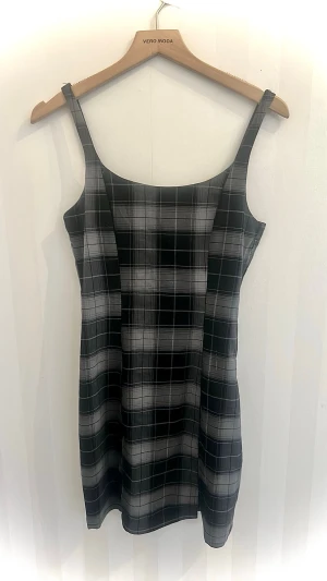 Rutig svart/grå kortklänning H&M Divided - Supersnygg kort klänning från H&M Divided i svart och grått rutigt mönster. Klänningen har smala axelband och en figurnära passform som ger en clean och trendig look. Perfekt att styla med en t-shirt under eller en stickad tröja över.