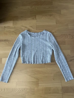 Grå ribbad croppad tröja från SHEIN - Grå ribbad långärmad tröja från SHEIN i croppad modell. Tröjan har en rund halsringning och är tillverkad i ett mjukt, stretchigt material som sitter snyggt på kroppen. Perfekt att styla med höga jeans eller kjol.