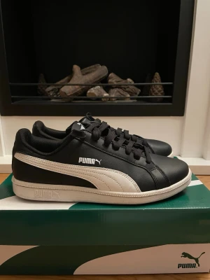 Svarta och vita Puma sneakers - Säljer ett par klassiska Puma sneakers i svart skinn med vita detaljer och vit sula. Skorna har snörning och den ikoniska Puma-loggan på sidan och tungan. 