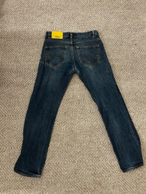 Mörkblå jeans från WESC med gul patch - Säljer ett par mörkblå jeans från WESC med klassisk gul patch bak och snygga kontrastsömmar. Bakfickorna har den ikoniska WESC-bågen i gult. Jeansen har en slim passform och är tillverkade i slitstarkt denimtyg. Storleken kommer i 27W och 30L. 