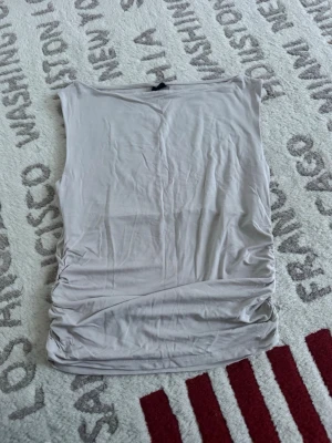 Beige ärmlös topp från Gina Tricot - Säljer en beige ärmlös topp från Gina Tricot i storlek L. Toppen har en slät design med snygga rynkade detaljer på sidorna och är gjord i mjukt bomullsmaterial. Perfekt att styla med jeans eller kjol för en chill look.