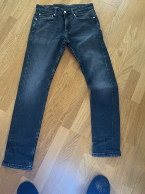 Svarta jeans Calvin Klein  - Snygga svarta jeans från Calvin Klein med diskret tvättad look. Modellen är slim fit med klassiska fem fickor och silverfärgade nitar. Jeansen har normal midja och är tillverkade i mjukt denimtyg för skön passform.