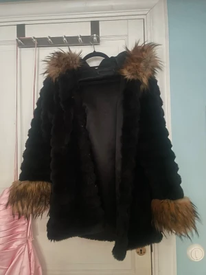 Svart pälsjacka med fuskpälsdetaljer - Säljer en svart pälsjacka med stora fluffiga fuskpälsdetaljer i brunt vid krage och ärmslut. Jackan har en oversized look och är perfekt för dig som vill sticka ut. Fodrad insida för extra komfort och värme. Supermysig och trendig till höst och vinter! Passar mig som är storlek S men funkar på M också.