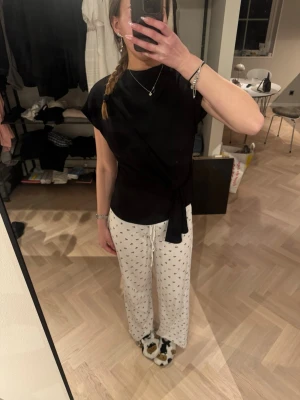 Svart omlottopp med knyt - Säljer en svart omlottopp med knyt i midjan. Toppen har korta ärmar och en stilren, figurnära passform som ger en snygg siluett. Perfekt att styla med både jeans och kjol för en trendig look.