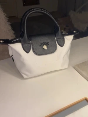 Vit och svart Longchamp handväska - Snygg väska från longchamp. Liten svart vit modell, axelband finns till. Den är köpt på Plick sedan innan men har inga tydliga tecken på användning 