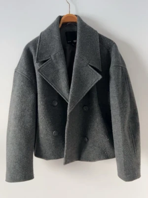 Grå kappa - Säljer en grå kappa från lager 157. Jackan är croppad och har en loose passform, perfekt att slänga på över en stickad tröja.