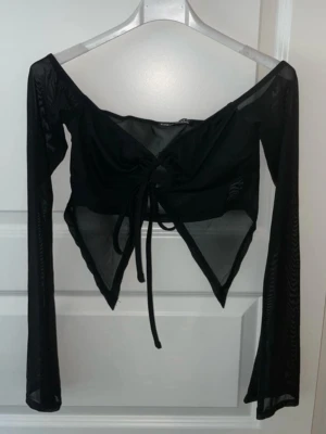 Svart mesh bolerotopp med snörning - Säljer en svart bolerotopp i mesh med långa ärmar och snygg snörning framtill. Toppen har en croppad passform och spetsig nederkant som ger en edgy look. Perfekt att styla över ett linne eller en bandeau för en trendig outfit.