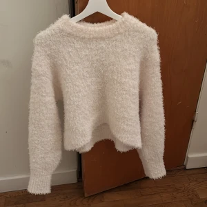 Vit fluffig stickad tröja - Supermjuk och fluffig vit stickad tröja med lång ärm och rund hals. Perfekt för kyliga dagar när du vill vara både varm och snygg. Tröjan har en lätt oversized passform och ribbade muddar vid ärmslut och nederkant.