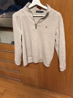 Beige half zip tröja från Polo Ralph Lauren - Säljer en beige långärmad tröja från Polo Ralph Lauren med half zip och liten broderad logga på bröstet. Tröjan har en mjuk bomullskänsla och klassisk krage. Perfekt för chill höst- och våroutfits.