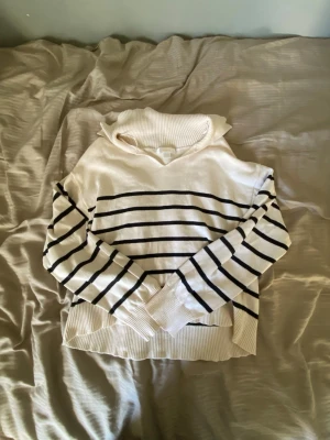 Vit och svart randig tröja Gina Tricot - Snygg vit stickad tröja från Gina Tricot med svarta horisontella ränder. Tröjan har långärmade ärmar, ribbad krage och muddar vid ärmslut och nederkant. Perfekt för dig som gillar klassisk stil med en modern twist.