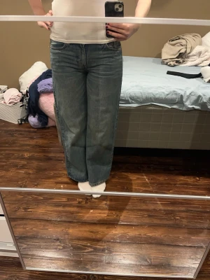 Blå wide jeans med normal passform - Säljer ett par blå jeans med breda ben och klassisk femficksdesign. Jeansen har normal passform och midwaist, tillverkade i jeansmaterial. Perfekta för dig som gillar en avslappnad och trendig look. Färgen är en tvättad blå med lätt slitning.