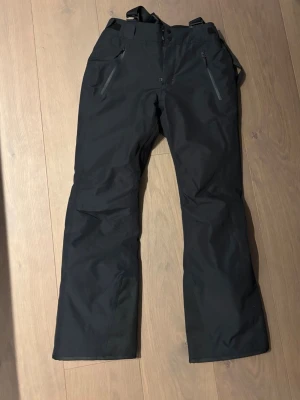 Svarta skidbyxor med hängslen - Säljer ett par svarta termobyxor ifrån Everest med justerbara hängslen och dragkedjor vid fickorna.Materialet vatten tåligt, vilket gör dem grymma för snö och kyla.