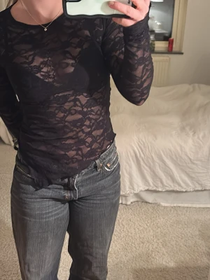 Svart spetsblus med lång ärm - Säljer en svart, transparent spetsblus med lång ärm. Blusen är tight och har ett blommigt spetsmönster som ger en snygg och trendig look. Perfekt att styla med jeans eller kjol för en cool outfit.