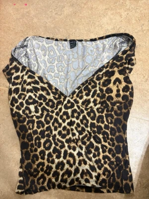 Leopardmönstrad omlottopp från SHEIN - Säljer en snygg leopardmönstrad omlottopp från SHEIN i storlek M. Toppen har v-ringad hals och är ärmlös, med figurnära passform. Materialet är mjukt och stretchigt polyester som sitter skönt mot kroppen. Perfekt för dig som gillar djurmönster och vill sticka ut.